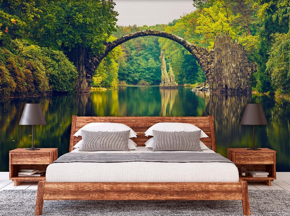 Bedroom - A modern bedroom with a large Decor2Go wallpaper mural of a picturesque scene featuring an ancient stone arch bridge over a calm river, surrounded by lush green forests. Two bedside lamps flank a bed with white bedding.