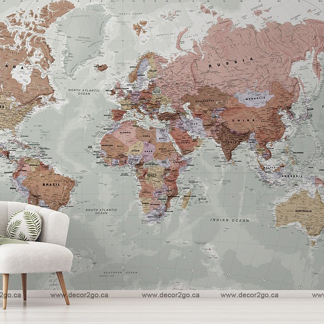 A stylish room with a large, detailed Decor2Go Colored World Map Wallpaper Mural. There's a modern white armchair with a green blanket, a small table with a plant, and a white floor lamp.