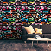Living Room - A modern living room with a gray sofa adorned with colorful pillows, in front of a vibrant wall covered in Decor2Go Wallpaper Mural's Coloured Cassette Wallpaper Mural. A white coffee table with a cup on it sits on a wooden floor.