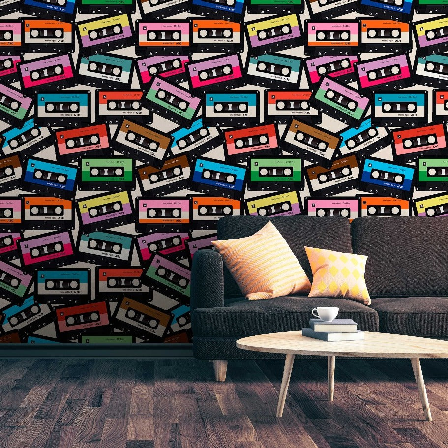 Living Room - A modern living room with a gray sofa adorned with colorful pillows, in front of a vibrant wall covered in Decor2Go Wallpaper Mural's Coloured Cassette Wallpaper Mural. A white coffee table with a cup on it sits on a wooden floor.