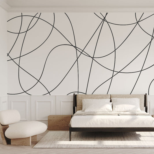 A minimalist bedroom featuring a large bed with white bedding and a wooden frame. The wall is adorned with the Decor2Go Wallpaper Mural's Contemporary Scribble Elegance, showcasing an artistic geometric pattern of black curved lines on a white background. To the left is a round chair, and natural light streams in through a large window with sheer curtains.