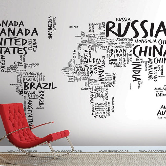 A modern red chair against a white wall featuring a Decor2Go Wallpaper Mural where countries' names form the shape of their geographic outlines. The map and chair are part of a stylish interior.