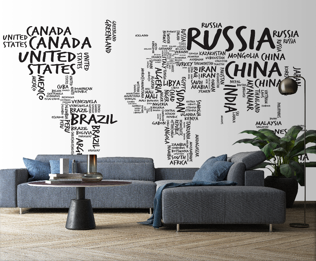 A modern living room with a large Decor2Go Wallpaper Mural Country Names Map on the wall where countries are represented by their names in different font sizes. The room has a blue sofa, a coffee table, and a p
