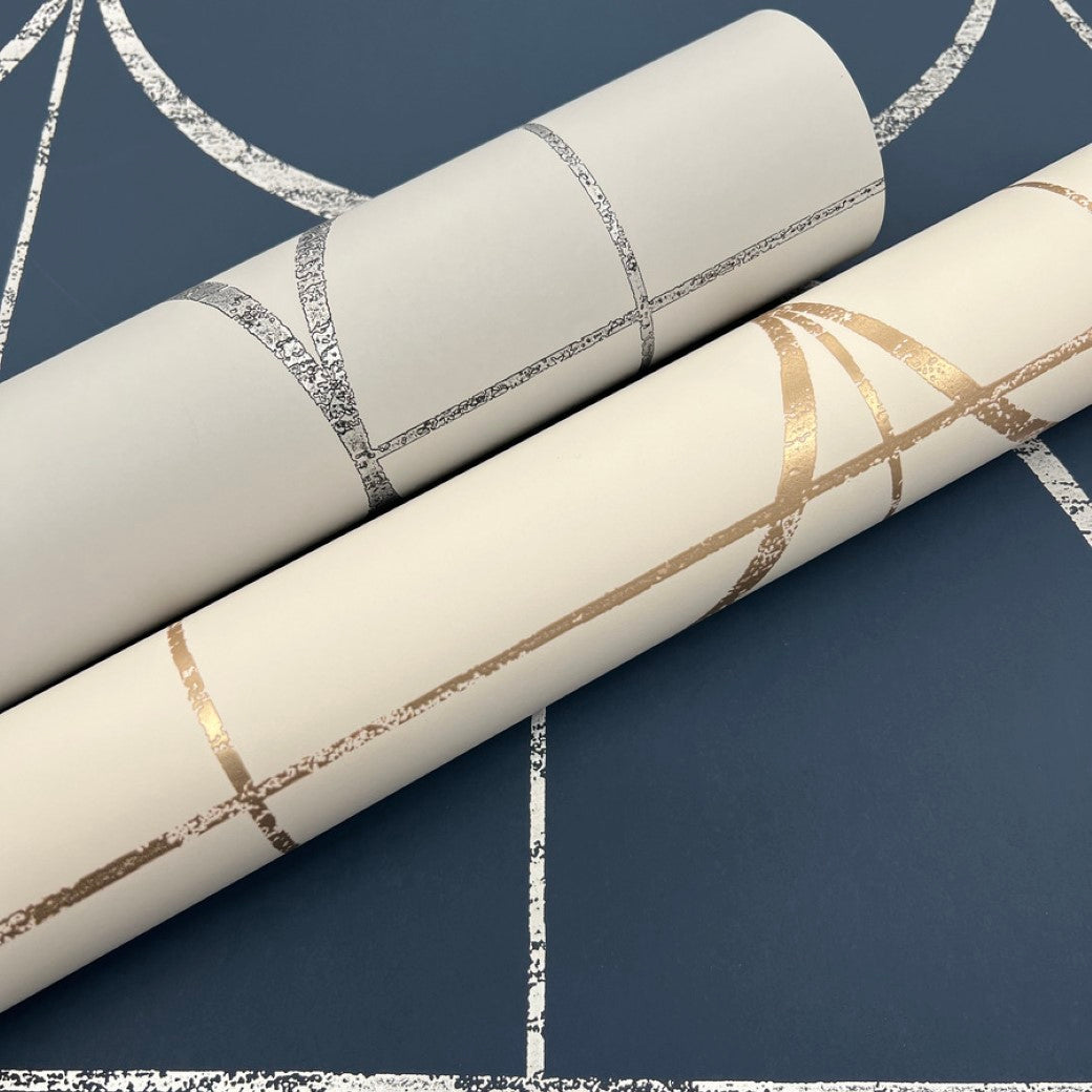Two York Wallcoverings' Cream & Gold Sprigs Wallpaper rolls from the Modern Metals Collection showcase curved geometric lines in metallic silver and gold on a cream base, set elegantly against a matching dark blue background.