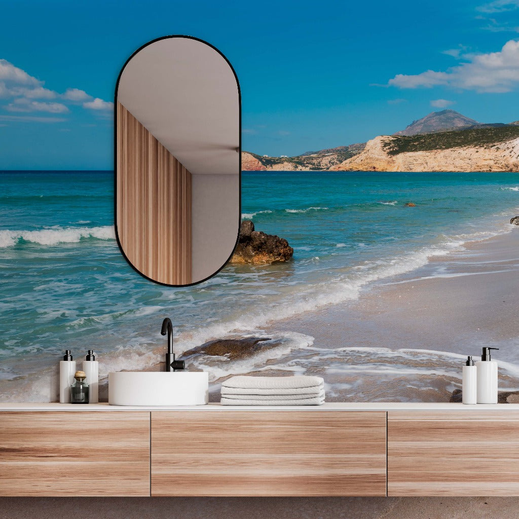 A modern bathroom vanity with a unique oval mirror is set against a backdrop of the serene Decor2Go Wallpaper Mural, showcasing clear blue water, white sands, and a sunny sky.