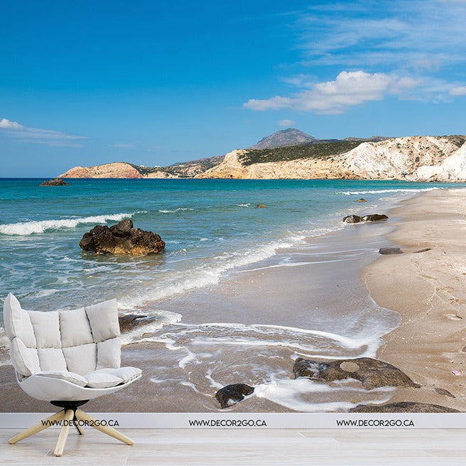 A surreal image of a comfortable white chair and side table with a plant positioned on a beach, seamlessly blending indoor comfort with the natural beauty of the seaside landscape at Decor2Go Wallpaper Mural.