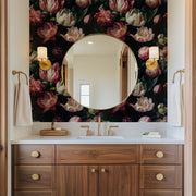 Bathroom - A bathroom features a circular mirror set against Decor2Go Wallpaper Mural's Dark Elegance Floral Wallpaper. A wooden vanity with gold fixtures holds a sink, soap dish, and towels. Two wall sconces enhance the charm, while a small window adds natural light.
