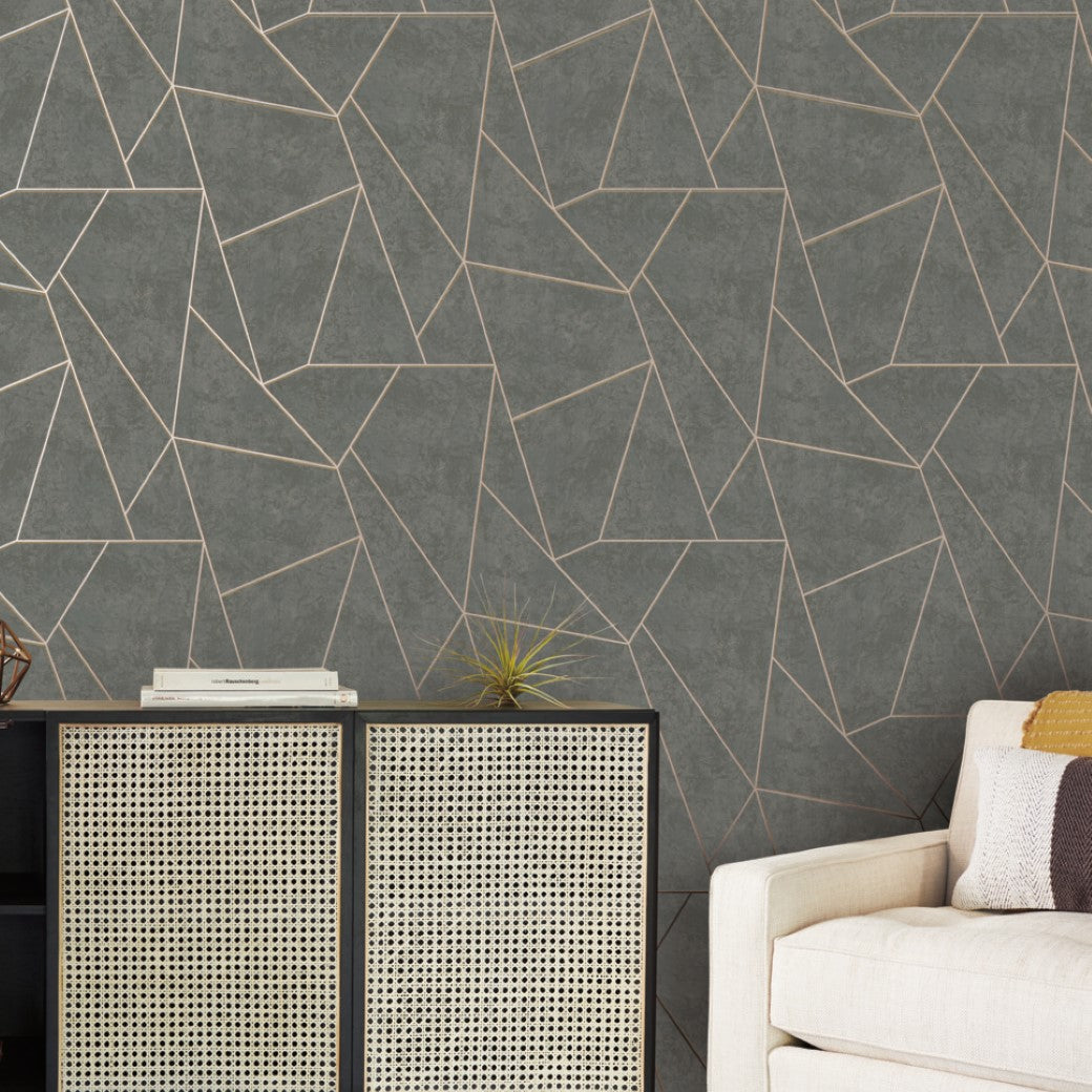 A modern living room features York Wallcoverings' Dark Grey & Gold Nazca Wallpaper, complemented by a cabinet with a cane front and a small plant. A beige sofa with a cushion is partially visible on the right, enhancing the chic aesthetic of the space.