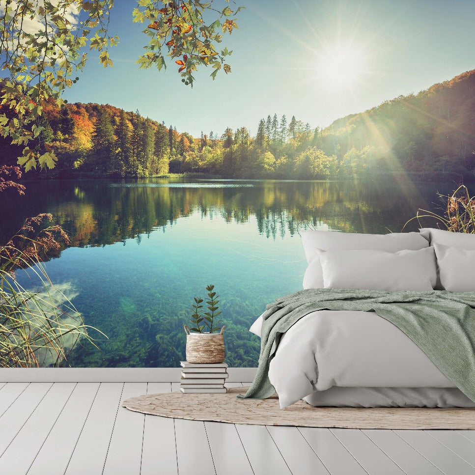 A luxurious outdoor bedroom setup with a plush bed and green linens overlooking a serene lake surrounded by lush forests under a sunny sky, complemented by rustic wooden furniture featuring the Day on The Lake Wallpaper Mural from Decor2Go Wallpaper Mural.