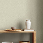 A wooden shelf with a tray, striped bowl, white ceramic vase, and books is set against York Wallcoverings Dew Drop Beige Wallpaper (60 SqFt) featuring a light beige background with a subtle dotted pattern.