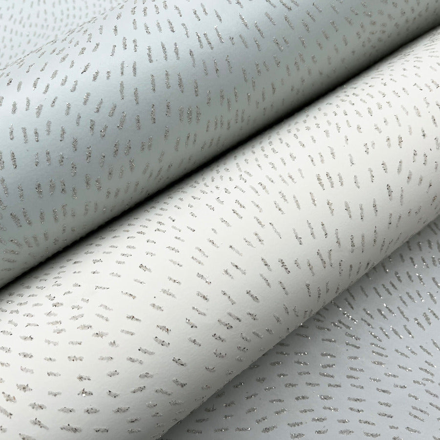 Close-up of Dew Drop Sea Mist Wallpaper by York Wallcoverings, featuring an irregular pattern of shimmering silver dashes on a subtle, light-toned background—reminiscent of glitter wallpaper.