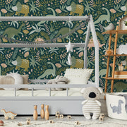 Bedroom - A cozy children's bedroom with a Dinosaur Wilderness Wallpaper Mural from Decor2Go Wallpaper Mural featuring colorful dinosaurs, a toddler bed, teddy bear, wooden toys, and a shelf with books and decorations.