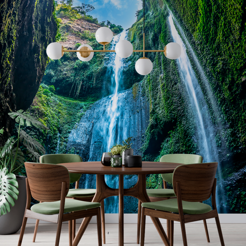 A modern dining room with a large Decor2Go Wallpaper Mural Elevated Waterfall Wallpaper Mural. The room features a wooden table, green upholstered chairs, a stylish chandelier, and a potted plant.