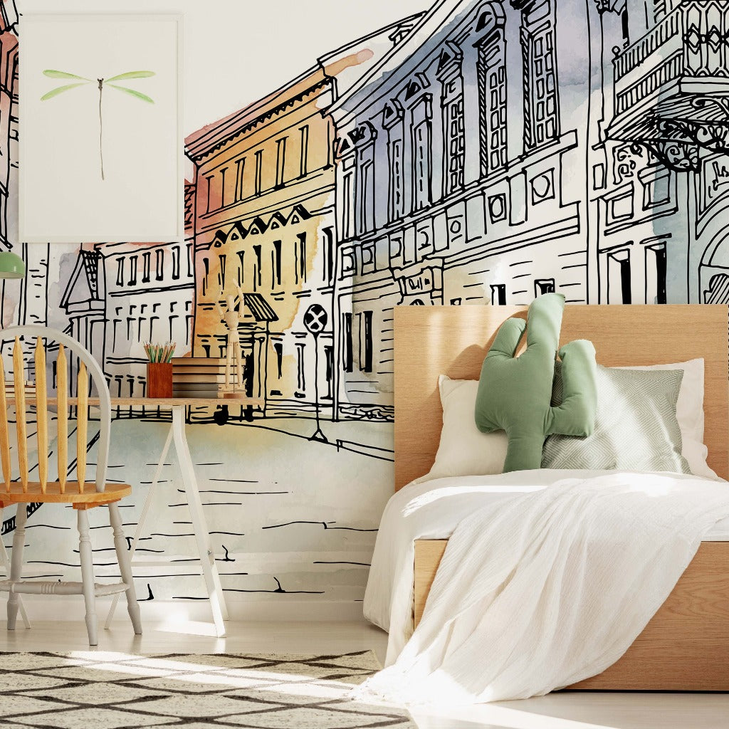 A creatively designed bedroom with one wall illustrated with a "European Alley Watercolor Wallpaper Mural" from Decor2Go Wallpaper Mural to resemble a colorful street scene, featuring architectural drawings of buildings. A wooden bed with white bedding and a wooden chair.