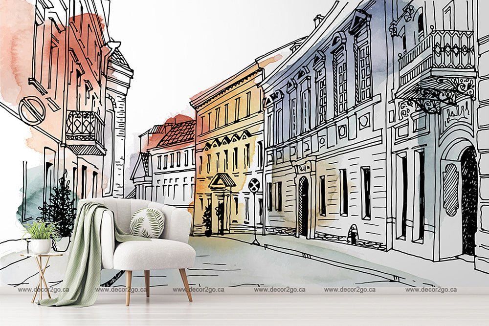 A stylish interior featuring a modern white chair with a green throw blanket in front of a large Decor2Go Wallpaper Mural depicting a colorful, sketch-style drawing of the European Alley Watercolor Wallpaper Mural.