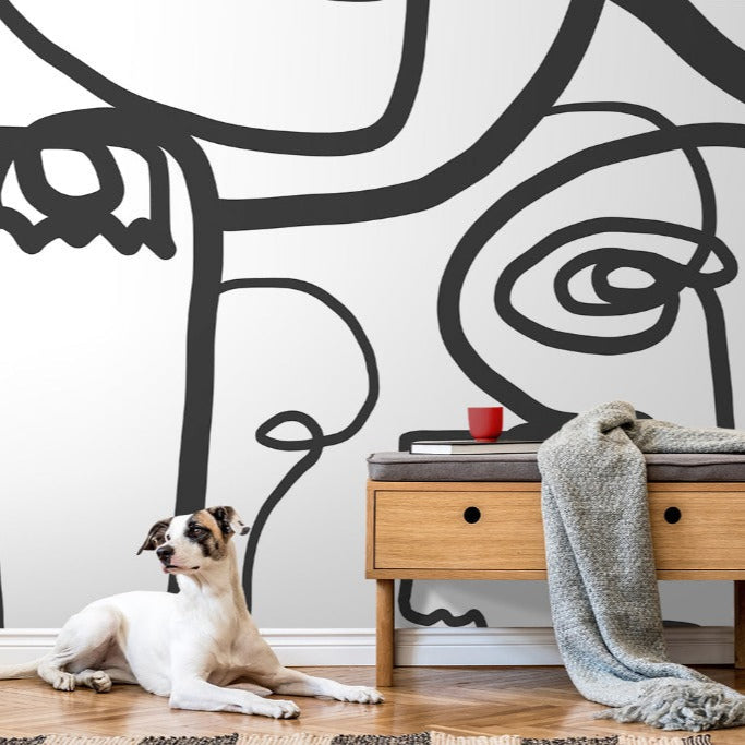 A stylish room featuring a large Face Art Wallpaper Mural from Decor2Go Wallpaper Mural on the wall, a wooden console table with a red mug atop, a draped grey blanket, and a plant. A white and brown dog lounges on