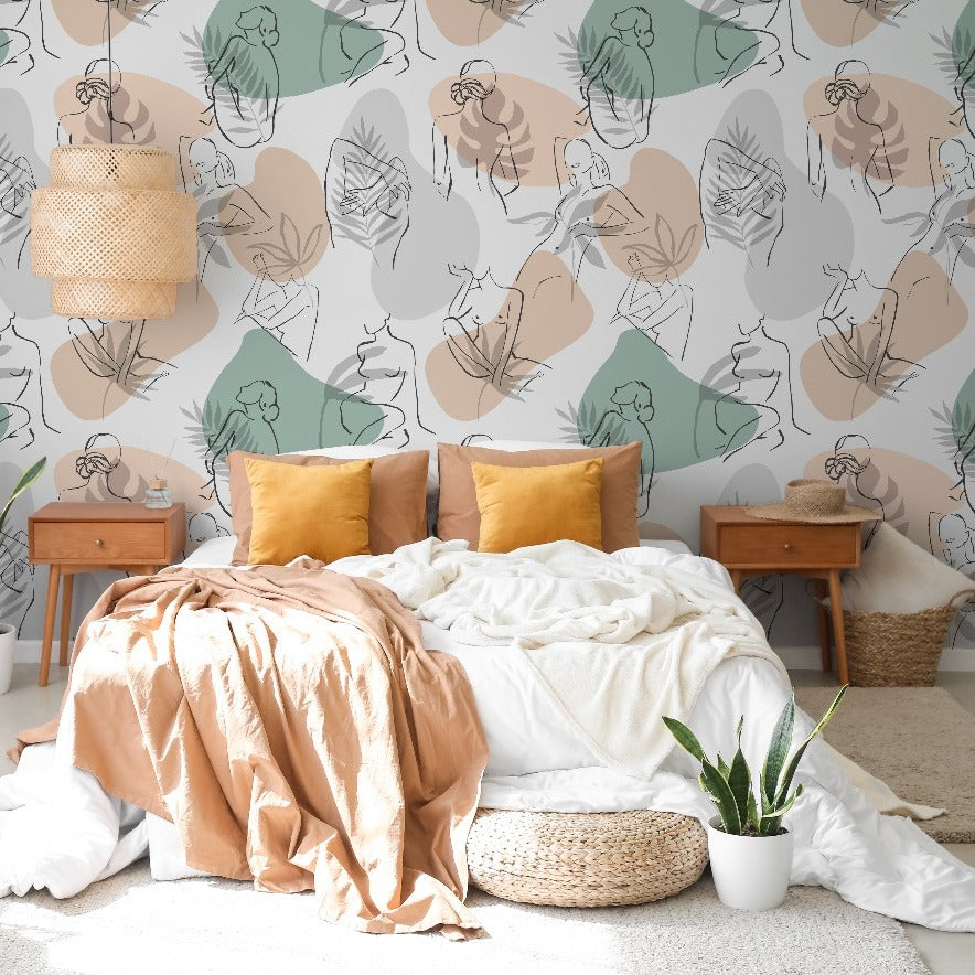 A cozy bedroom with a Feminine Form Wallpaper Mural from Decor2Go, covering the walls around a tousled white bed covered in a beige throw. The bed is flanked by wooden nightstands and the room features modern elegant decor including a woven lamp and green plants.