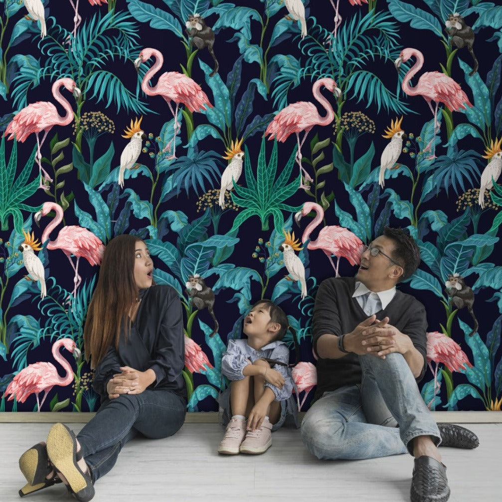 A family consisting of a woman, a man, and a young child sitting and looking at each other joyfully against a vibrant Flamingo Fever Wallpaper Mural with plants by Decor2Go Wallpaper Mural.