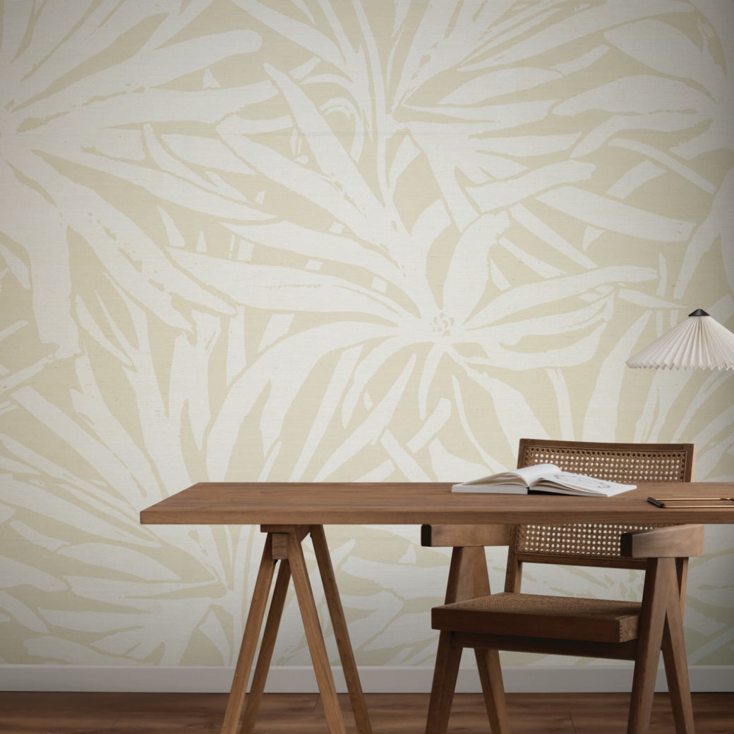 A minimalist workspace with a wooden desk, chair, open book, and lamp. The beige wall features York Wallcoverings' Floral Canopy Beige Wallpaper Mural (Panels), adding bold abstract botanical patterns for visual interest.