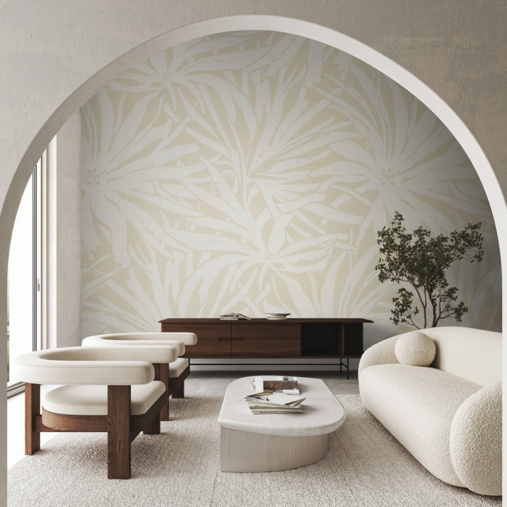 A modern living room with cream armchairs, a curved sofa, wooden sideboard, minimalist coffee table, and York Wallcoverings' Floral Canopy Beige Wallpaper Mural on a feature wall, viewed through an arched doorway.
