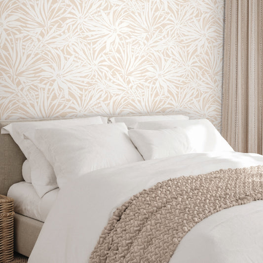 A cozy bed with white bedding and a beige knitted throw, set against York Wallcoverings' Floral Canopy Blush Wallpaper. Beige striped curtains hang nearby, and a wicker basket sits next to the bed.