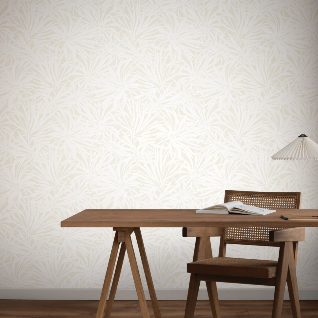 A minimalist workspace with a wooden desk and chair, an open book, and a modern white lamp. The background features York Wallcoverings’ Floral Canopy Cream Wallpaper (60 SqFt) with a light leafy pattern.