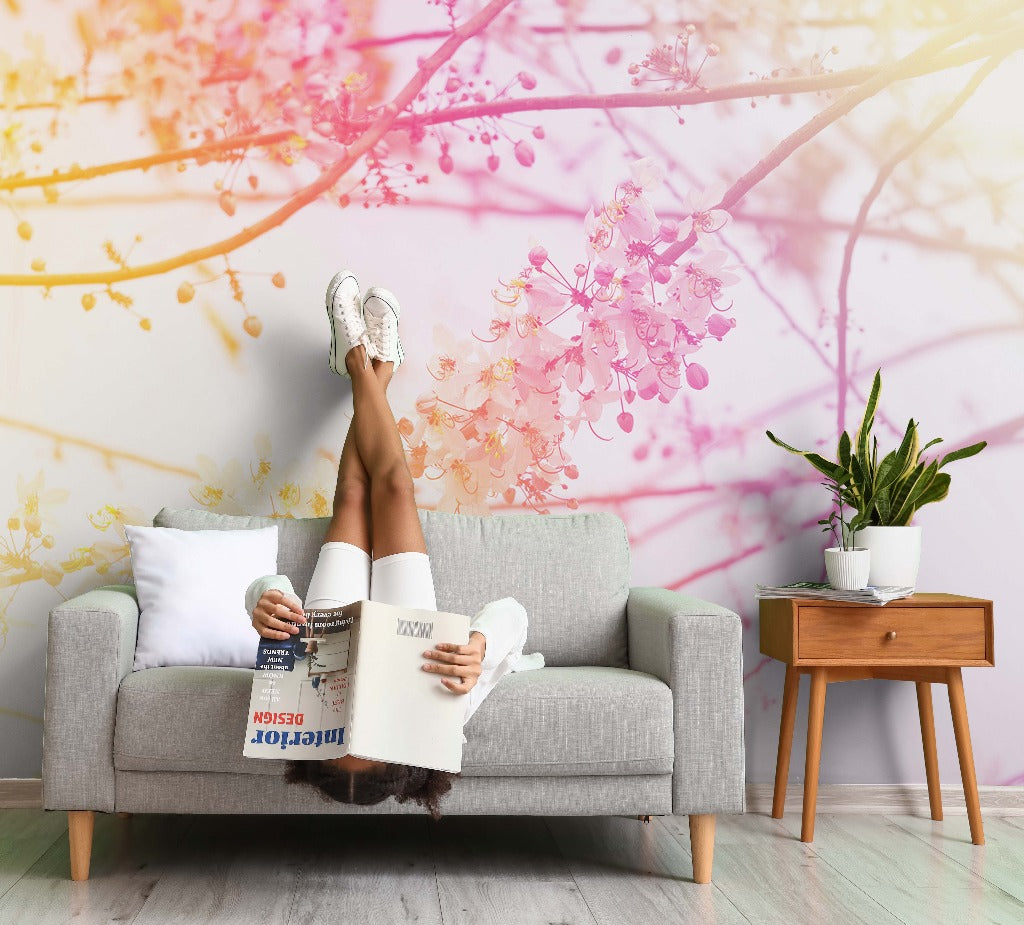 A person lounging on a gray sofa, legs raised against a vibrant Decor2Go Wallpaper Mural, reading a magazine titled "interior design," beside a wooden side table with a potted plant.