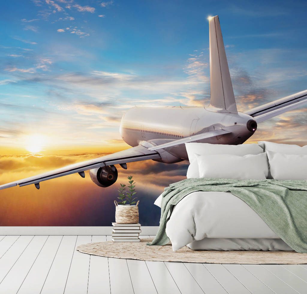 An airplane flying low over a cozy bedroom setup with a bed, linens, and a small plant, set against the Decor2Go Flying Above the Clouds Wallpaper Mural sky, symbolizing travel dreams or jet-set lifestyle.