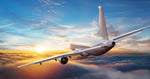 A passenger airplane flies above the clouds during sunset, creating a stunning Flying Above the Clouds Wallpaper Mural by Decor2Go Wallpaper Mural. The sky is a mix of orange, yellow, and blue hues as the sun sets on the horizon, illuminating the clouds with a warm glow. The aircraft is angled slightly upward, appearing to ascend.