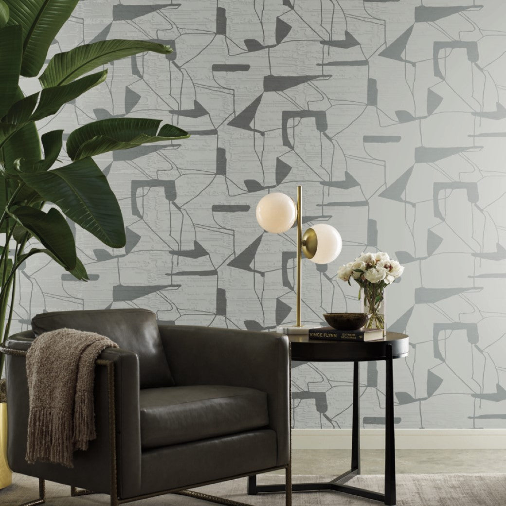 Living Room - modern , a gray armchair sits next to a side table with a spherical lamp and vase of flowers. The walls feature York Wallcoverings' Fog & Silver Abstract Geo Wallpaper, accented by a large plant on the left for sleek minimalism