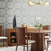 Dining Room - A modern showcases a round wooden table, four white-cushioned chairs, and a sideboard. A decorative vase and potted orchid add flair, while the York Wallcoverings' Fog & Silver Sun Circles Wallpaper enhances geometric designs, complemented by a gold chandelier