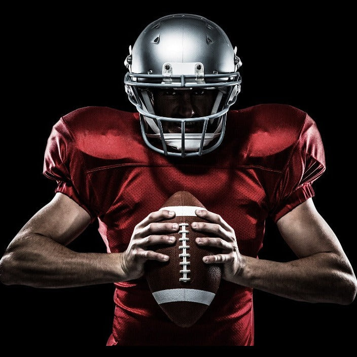 Decor2Go Wallpaper Mural of a football player in a red jersey and silver helmet holding a football, intensely looking forward, illuminated dramatically against a dark background.