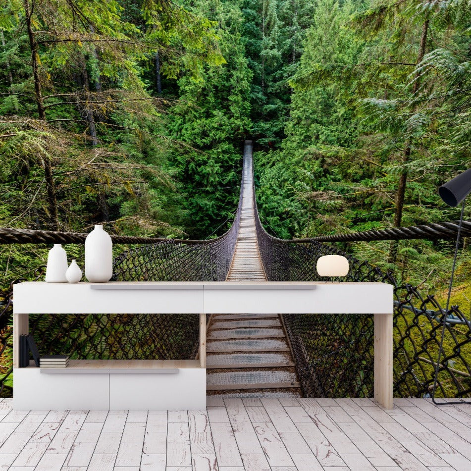 A sleek, modern desk with decorative items in front of a Forest Suspension Bridge Wallpaper Mural by Decor2Go blurs the line between indoor and outdoor settings.