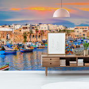 Living Room - A vibrant living room with a scenic Forever Malta Wallpaper Mural from Decor2Go Wallpaper Mural of a Mediterranean coastline featuring colorful boats and historic architecture. A modern sideboard and lamp complete the decor.