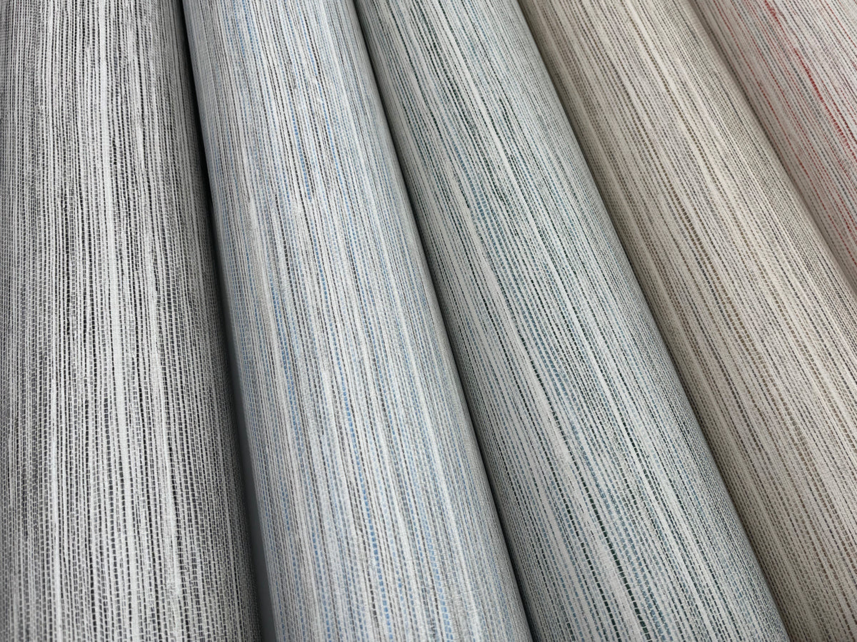 A close-up view of five fabric rolls displayed vertically, showcasing a spectrum of colors including shades of gray, blue, and beige. The fabrics have a subtle textured pattern, giving them a slightly woven appearance reminiscent of Fountain Grass Smokey Blue Wallpaper Blue (60 Sq.Ft.) by York Wallcoverings for a natural aesthetic.