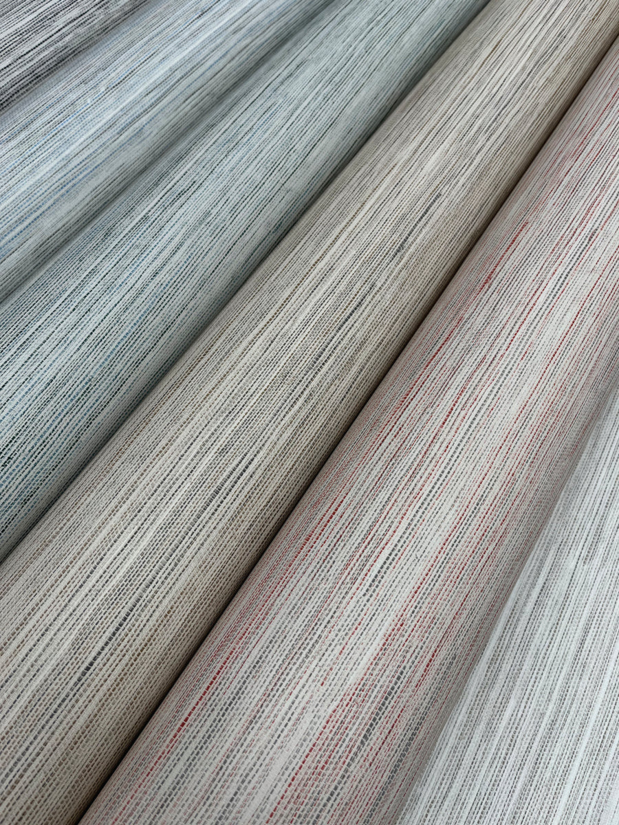 Close-up image of four rolls of fabric arranged side by side. Each roll features a subtly striped pattern with hints of various colors like grey, beige, blue, and a touch of red. The texture suggests a woven material with fine, interlacing threads that offer a natural aesthetic reminiscent of York Wallcoverings' Fountain Grass Camel Wallpaper Brown (60 Sq.Ft.).