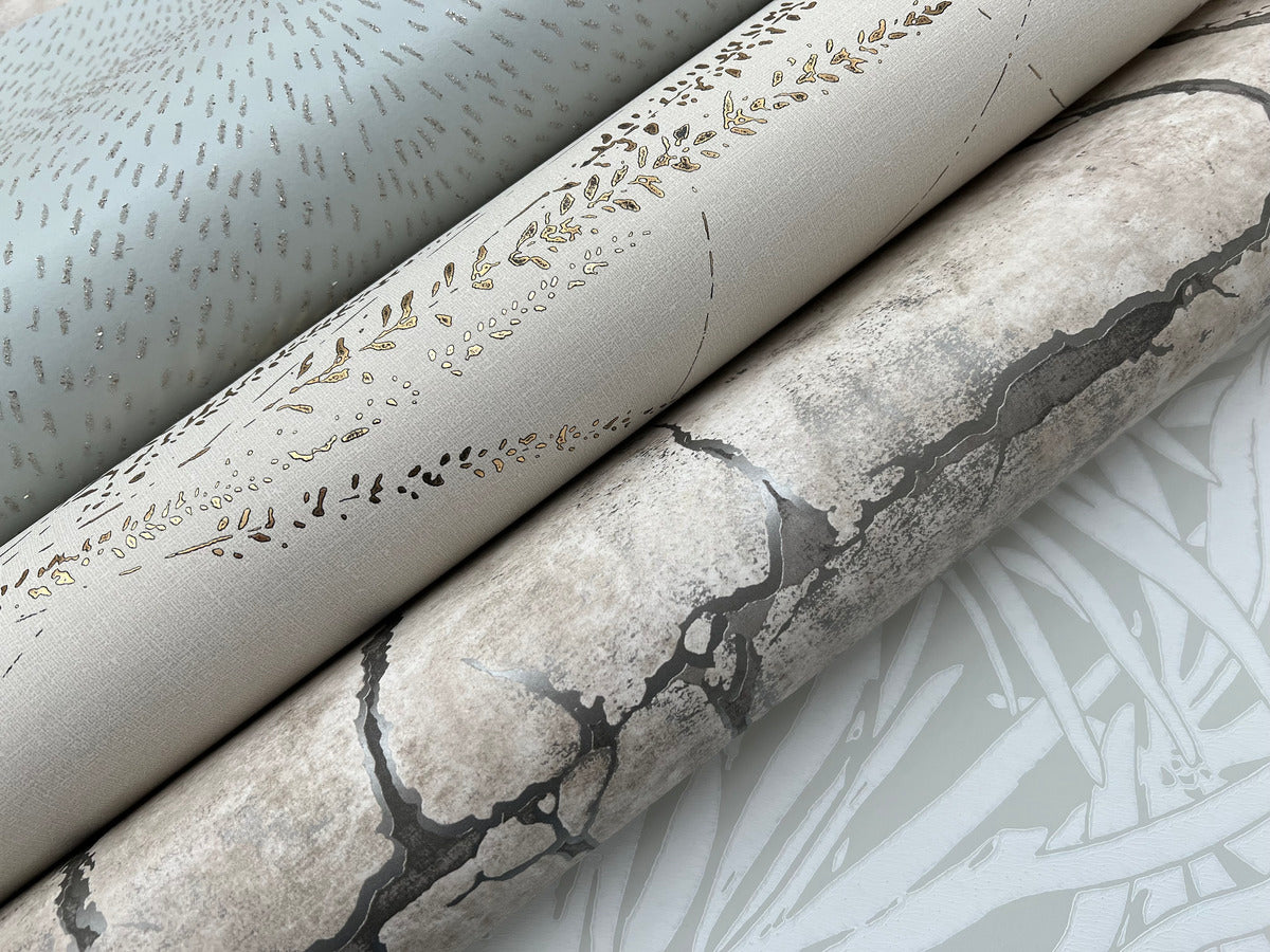 Three wallpaper rolls, including York Wallcoverings' Graceful Willow Pale Straw Wallpaper (60 SqFt), a gold and beige botanical damask, and a cracked stone design, are displayed side by side on a light surface.
