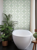 A modern bathroom features a white oval bathtub with sleek fixtures. The wall behind the tub displays York Wallcoverings' Garden Trellis Rain Wallpaper Blue, Grey (60 Sq.Ft.), offering easy installation and removal. Several potted plants, including a large leafy one on the left, add botanical elegance to the space.