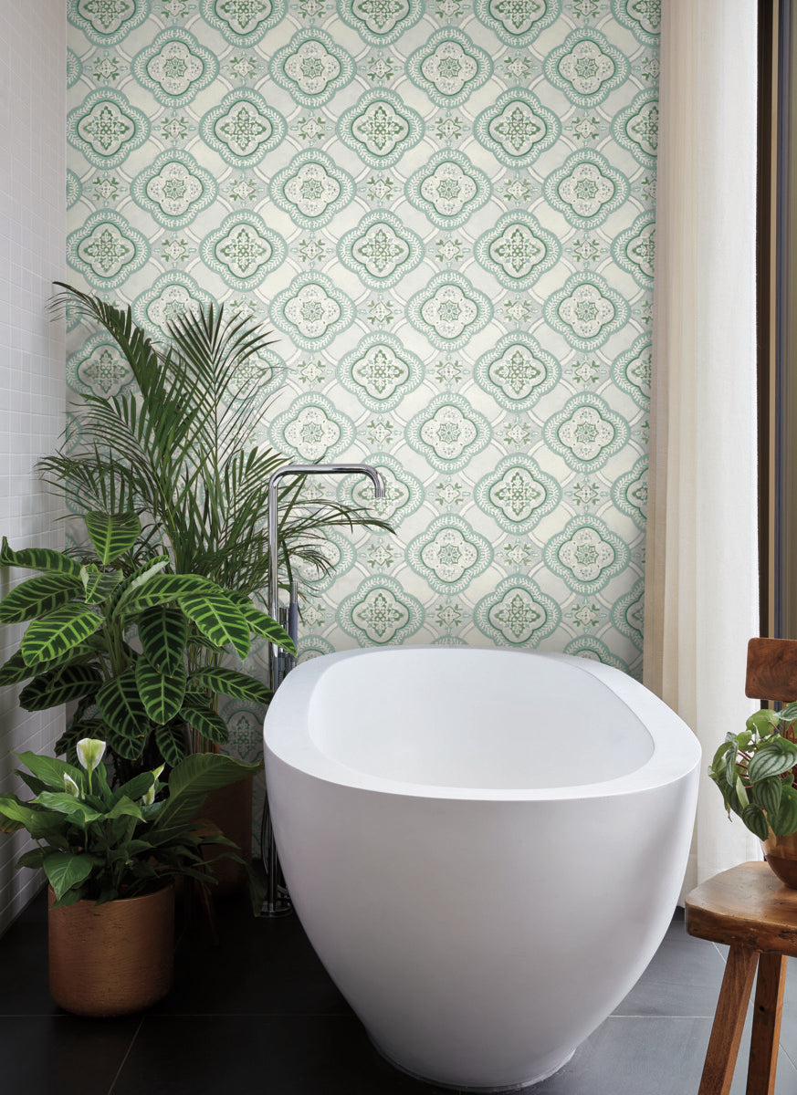 A modern bathroom features a white oval bathtub with sleek fixtures. The wall behind the tub displays York Wallcoverings' Garden Trellis Rain Wallpaper Blue, Grey (60 Sq.Ft.), offering easy installation and removal. Several potted plants, including a large leafy one on the left, add botanical elegance to the space.