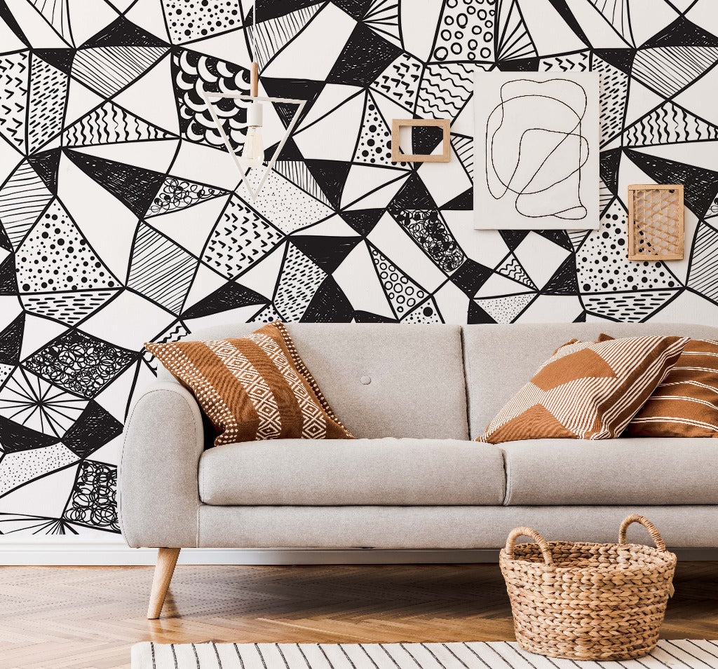 A modern living room featuring a gray sofa with patterned cushions, a wicker basket, and a striking Decor2Go Geometric Black & White Wallpaper Mural.
