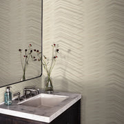Bathroom - A stylish corner featuring a marble sink, modern faucet, and a mirror reflecting a vase with red flowers. The walls are adorned with York Wallcoverings' Glistening Chevron Wallpaper Blonde (56 sq.ft.) showcasing a subtle geometric pattern