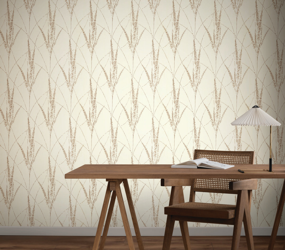A wooden desk with an open notebook and lamp stands before York Wallcoverings' Graceful Willow Cotton Wallpaper, featuring a cream-colored botanical damask with a vertical wheat pattern. A wooden chair with a woven back is at the desk.