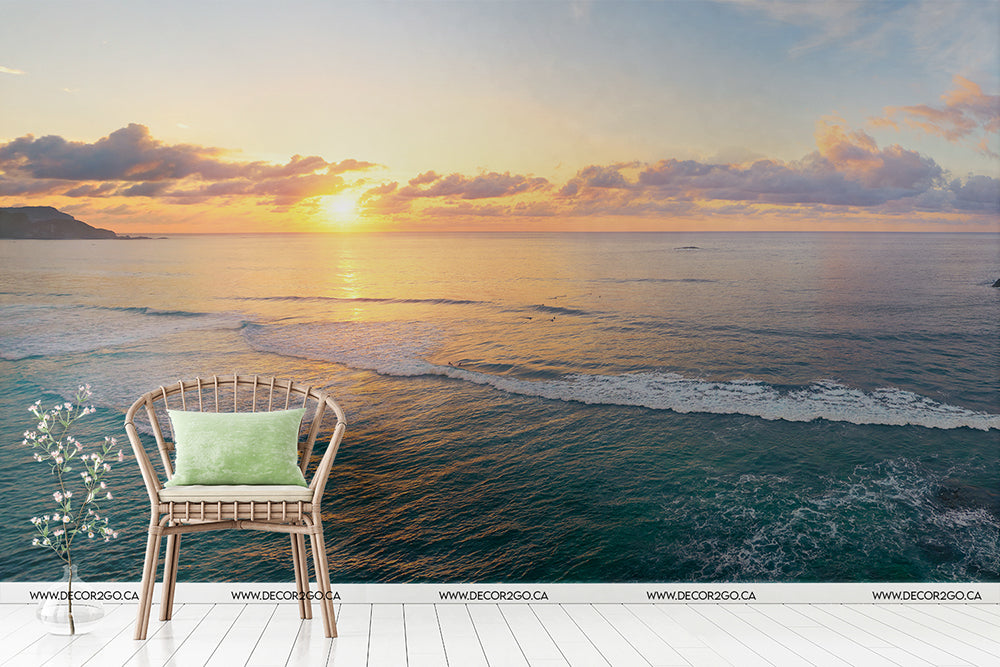 A serene Great Blue Sea Wallpaper Mural view at sunset from a balcony with a single wicker chair facing the calm sea, enhanced by the warm glow of the sun near the horizon by Decor2Go Wallpaper Mural.