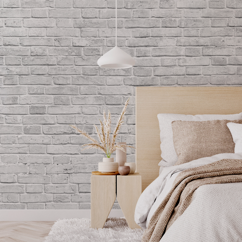 A cozy bedroom corner featuring a neatly made bed with a beige headboard and knit throw, a wooden side table with a vase of dried plants, under a pendant light against the Decor2Go Wallpaper Mural background.