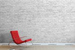 A minimalist room with a Decor2Go Great White Wall Wallpaper Mural and a vibrant red modern chair against it. The floor is simple, light grey, adding contrast to the scene.