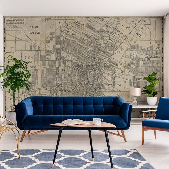 A stylish living room with a large Decor2Go Wallpaper Mural of Greater Winnipeg as wallpaper, featuring a dark blue sofa, a golden wire lounge chair, a coffee table, and a side table with plants.