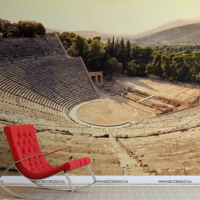 A modern red lounge chair placed in the ancient Greek architecture of a circular Epidavros Theater surrounded by lush green trees under a clear sky. The image marries contemporary and historical elements.