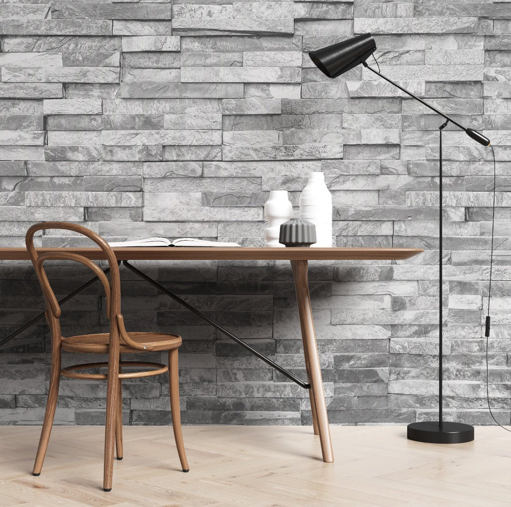 A modern workspace featuring a bentwood chair and a round table with a notebook and ceramic vases under a floor lamp, against an Grey Stone Wall Wallpaper Mural by Decor2Go Wallpaper Mural.