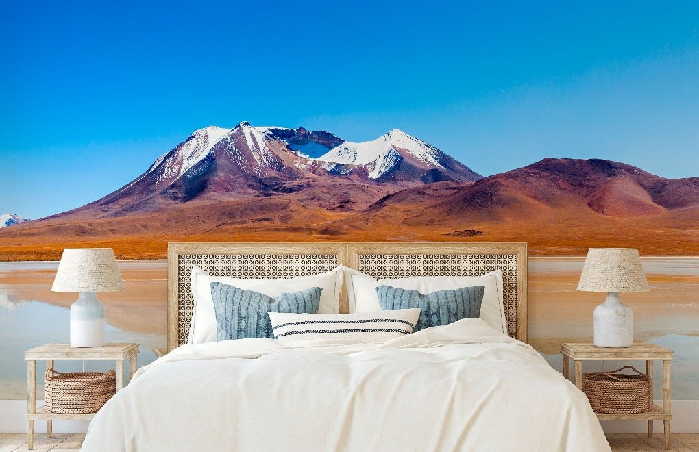 A luxurious bedroom with a large bed and elegant decor, set against a stunning backdrop of a "Decor2Go Wallpaper Mural" depicting a vivid landscape with a reflective orange lake and snow-capped mountains under the Heaven’s Summit Wallpaper Mural.