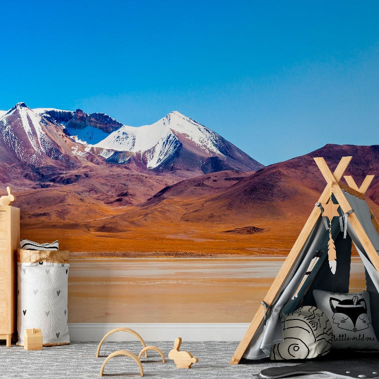 A child's bedroom with a playful teepee, wooden toys, and a dresser set against a custom-sized wall mural of snow-capped mountains and orange hills featuring the Heaven’s Summit Wallpaper Mural from Decor2Go Wallpaper Mural.